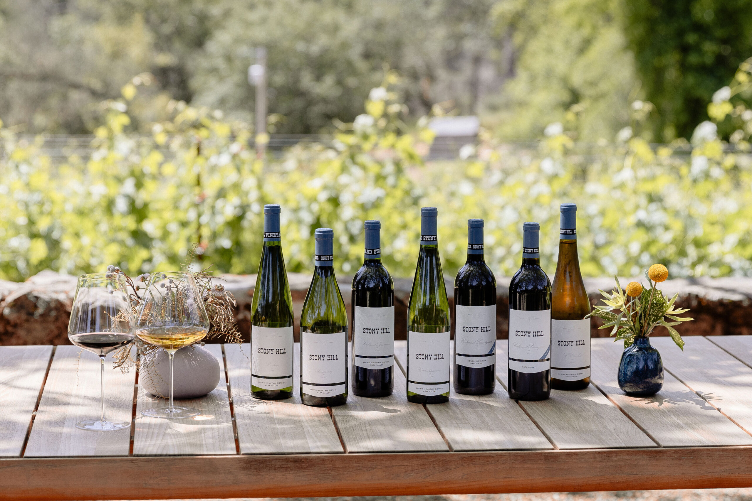 A collection of Stony Hill wines displayed on a table outdoors with two glasses of wine.