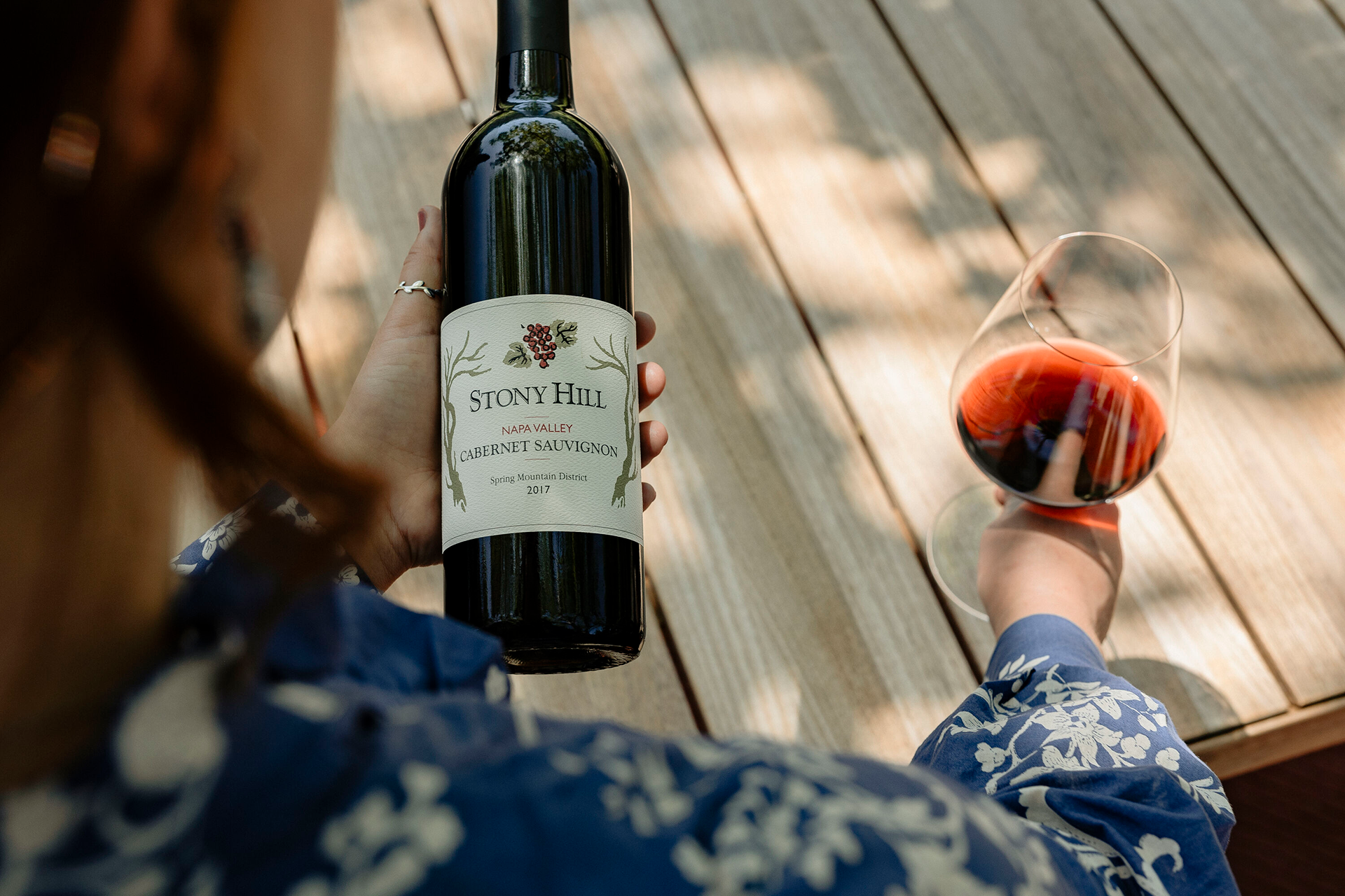 A guest holding a bottle of Stony Hill Cabernet Sauvignon in one hand, and a glass of wine in the other hand.