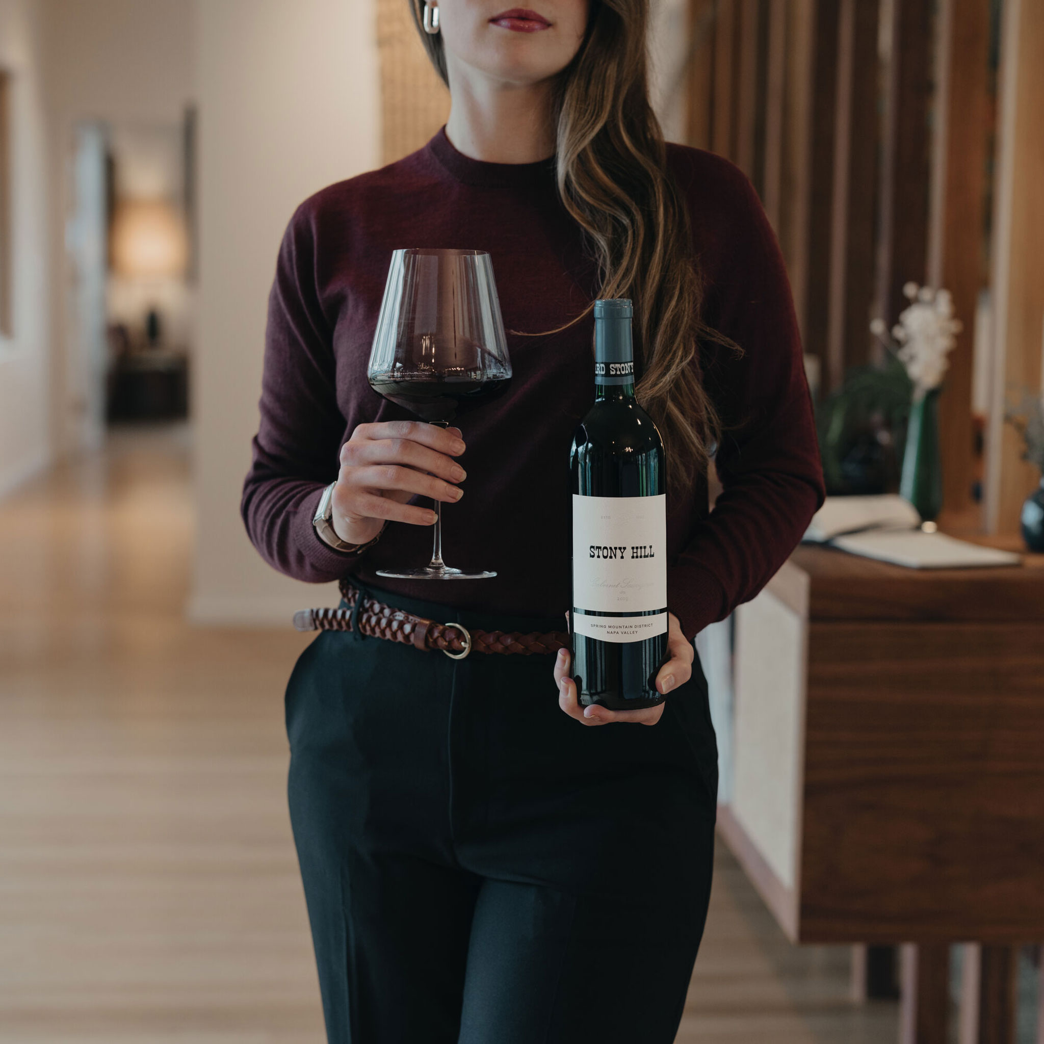 A bottle of Stony Hill Cabernet Sauvignon being held by a women with a glass in her other hand.