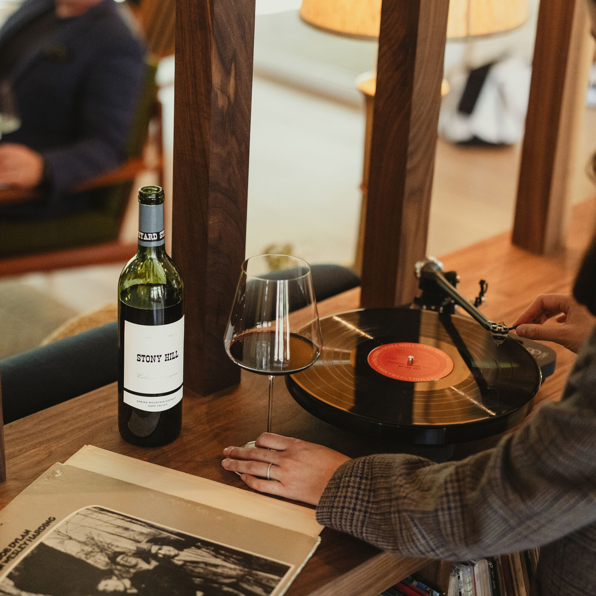 Inside The Residence at Stony Hill, a member looking at the record player and hold a glass of wine.